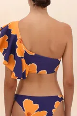 Top de bikini asimétrico con un solo hombro, estampado con flores naranjas sobre fondo azul marino y volado grande en el hombro.