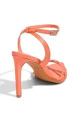 Sandalia de tiras finas color naranja coral, con punta cuadrada y taco alto. Posee una tira fina ajustable con hebilla alrededor del tobillo.