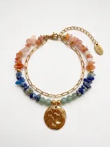Pulsera doble dorada de acero con piedras naturales facetadas en tonos rosados, azules y verdes, con dije metálico circular texturizado y cadena de extensión.