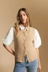 Chaleco tejido sin mangas color beige, con cuello redondo, botones frontales y punto calado con textura.