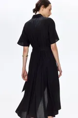 Vestido midi negro con cuello camisero, botonadura frontal de botones dorados, mangas cortas y cinturón ajustable para atar en la cintura.
