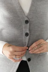 Chaleco tejido de punto en color beige, con escote en V, cierre frontal con botones oscuros y bolsillos frontales decorativos.