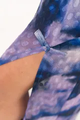 Vestido largo de manga larga con terminación campana, de color azul y violeta con estampado tie-dye, cuello mao con ojal y tajo frontal. Cuenta con flecos en el ruedo y tajo en la pierna.