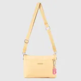 Cartera tipo bandolera de tamaño pequeño en color amarillo pastel, confeccionada en material sintético suave y engomado. Cuenta con una correa larga ajustable con el logo de la marca estampado, cierre superior y un dije colgante con la letra B en color rosa.