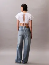 Remera cropped de algodón con corte boxy, cuello redondo y mangas cortas. Presenta un bajo redondeado en la parte delantera y un pequeño bordado de la marca en la manga.