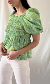 Blusa verde con estampado floral en tonos celeste y marrón, escote cuadrado con elástico, mangas cortas abullonadas y cuerpo fruncido.