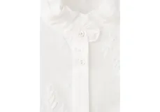 Blusa blanca de algodón con bordados florales, cuello alto con volados y mangas largas abullonadas con puños ajustados.