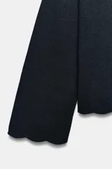 Chaqueta de punto color azul marino, con cuello solapa, manga larga y cierre frontal con botones metálicos. Presenta terminaciones en ondas en el bajo y los puños.