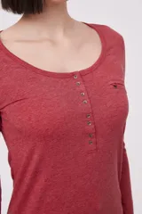 Remera blanca de manga larga, entallada, con cuello redondo y una hilera de botones en el frente. Incluye un pequeño bolsillo decorativo en el pecho.