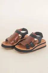 Sandalias de cuero color marrón con plataforma de madera y suela de goma negra. Tiras anchas de cuero marrón en el empeine y tobillo con ajuste de hebilla.