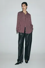 Camisa de manga larga con cuello clásico, cierre frontal abotonado y puños con botones. Presenta un diseño de rayas verticales en tonos bordó y crema, con bajo redondeado.