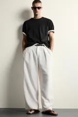 Pantalón relaxed fit de color blanco off-white, confeccionado en tejido con lino. Cuenta con pliegues frontales en la cintura, bolsillos delanteros y cierre frontal con cremallera y botón.