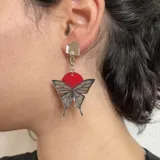 Par de aros colgantes con forma de mariposa plateada con detalles en negro y círculo superior rosa.