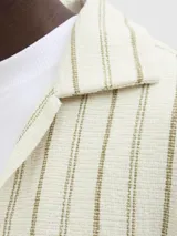 Camisa de manga corta a rayas verticales color crudo y verde, con cuello resort, corte holgado y cierre frontal con botones.