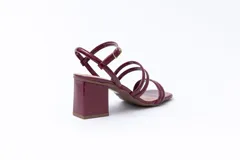 Sandalias de tacón cuadrado medio, confeccionadas en charol rojo. Presentan un diseño de tiras tubulares sobre el empeine y cierre con pulsera ajustable al tobillo mediante hebilla metálica.