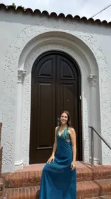 Vestido largo con estampado tie-dye en tonos violeta y fucsia, escote en V con detalles bordados dorados, cut-outs laterales bajo el busto y tirantes finos que se cruzan y atan en la espalda.