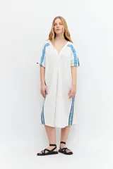 Túnica blanca de lino con corte oversized, escote en V, cierre con botones y mangas cortas. Presenta bordados geométricos azules en hombros y laterales.