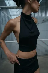 Conjunto de dos piezas compuesto por un top negro con cuello halter y una minifalda negra con diseño drapeado.