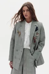 Blazer gris con estampado de cuadros, de doble botonadura, bolsillos delanteros y solapas de muesca. Viene decorado con múltiples pins metálicos en ambas solapas y un pañuelo estampado en el bolsillo del pecho.