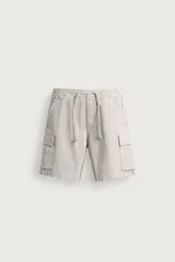Bermuda cargo relaxed fit de algodón con elasticidad y efecto lavado, color beige. Cuenta con cintura elástica ajustable con cordón, bolsillos frontales, bolsillos traseros de vivo y bolsillos plastrón con solapa en los laterales de las perneras.