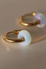 Par de aros tipo argolla dorados de acero quirúrgico, con una piedra natural de color gris translúcido colgando de cada uno.