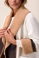 Saco de corte largo en color blanco, con solapas amplias y puños decorados con textura de corderito en color tostado. Presenta detalles en cuero sintético marrón en la parte frontal y en los puños, además de bolsillos laterales.