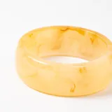 Brazalete rígido de resina en tono amarillo traslúcido con efecto jaspeado.