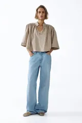 Blusa capa color beige con cuello alto, hombreras y diseño acampanado con frunces.