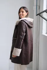 Tapado de cuero sintético color chocolate con interior y bordes de corderito sintético color beige. Presenta capucha, cierre frontal y bolsillos laterales.