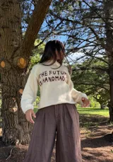 Sweater de lana merino virgen color crudo, con calce oversize y relajado. Presenta un bordado artesanal en el frente con la frase 'The Future Is Handmade' en color marrón.