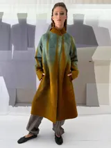 Tapado largo de fieltro de lana merino con teñido artesanal tie-dye en degradé de azul. Tiene cuello alto, cierre lateral con broches ocultos, bolsillos laterales y corte amplio.