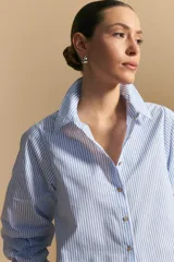 Camisa azul a rayas blancas, de manga larga con puños elastizados, entallada en la cintura y con cierre de botones frontales.