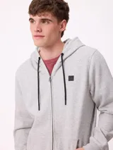 Campera canguro de felpa color gris claro melange, con capucha ajustable mediante cordones negros, cierre frontal completo, bolsillos tipo canguro y parche con logo de la marca en el pecho.