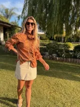 Camisa color marrón claro confeccionada en lino metalizado, con volados en el frente y cuello, mangas largas y botones ocultos. Corte holgado, más larga en la parte trasera.