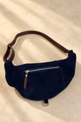 Riñonera urbana de cuero color tostado con cierre metálico superior, correa ajustable de cuero y detalle de placa metálica con logo en el frente.