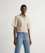 Camisa de tricolina color beige de la marca Cortelle, con cuello camisero y mangas cortas. Presenta un diseño con recortes frontales horizontales y cierre central con botones diferenciados.