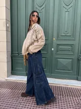 Campera tipo bomber de gamuza color beige, con diseño bordado de flores y motivos geométricos en blanco y negro. Presenta cuello clásico, cierre frontal con botones a presión y puños y ruedo de tejido elástico acanalado.