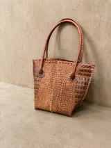 Cartera de cuero con textura crocco en color rojo, de silueta estructurada, manijas largas marrones y detalles de terminación artesanal en el borde superior.