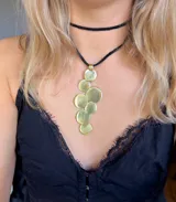 Collar con cadena de cuero negro y dije de bronce dorado con forma de racimo de círculos.