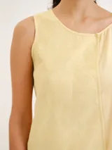 Blusa sin mangas de color amarillo claro, con diseño asimétrico en capas y detalles de tirantes finos en los hombros.