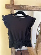 Top negro de textura gofrada, con escote en V cruzado, mangas cortas con volados y cintura fruncida con cordón ajustable.