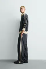 Sudadera de corte relajado en color azul marino con cuello alto y cierre frontal de cremallera. Presenta bandas laterales en color crema a contraste que recorren las mangas, puños y bajo en tejido rib, y bolsillos laterales de vivo.