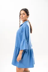Vestido corto azul, estilo camisero, con cuello camisero, cierre frontal con botones y mangas acampanadas con volados. Presenta un diseño holgado con cortes fruncidos en el cuerpo.