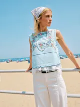 Top celeste sin mangas de algodón con escote cuadrado, bordado floral multicolor y líneas decorativas oscuras. Presenta un ruedo festoneado y laterales abiertos con tiras para ajustar.