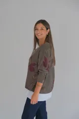 Sweater de corte amplio con diseño de doble capa, que presenta una capa superior en tono chocolate con estampado floral y una capa inferior en color blanco. Posee escote en V y mangas largas con terminaciones desflecadas.