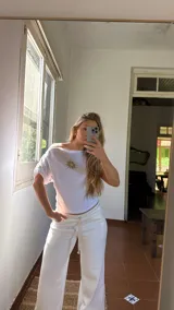 Remera blanca de algodón con cuello bote y detalle de elástico en los hombros. Presenta un estampado central de un sol en color dorado.