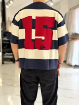 Remera de punto a rayas horizontales en tonos azul marino y beige, de manga corta y corte oversize. Presenta un gran número 15 rojo estampado en la espalda.