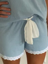 Pijama celeste de algodón acanalado compuesto por una remera de manga corta con escote en V adornado con puntilla blanca, y un short a juego con elástico y lazo de ajuste en la cintura.