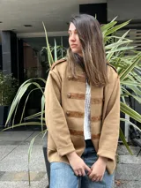 Chaqueta de abrigo color tostado, estilo militar, con detalles de apliques en cuerina marrón en los hombros, el cuello y las presillas frontales con botones metálicos dorados.