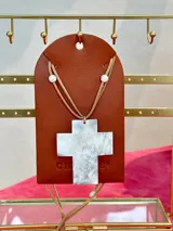 Collar con dije de cruz de guampa blanca, engarzado con hilo dorado. El collar es de cuero marrón con cuentas de piedra blanca.